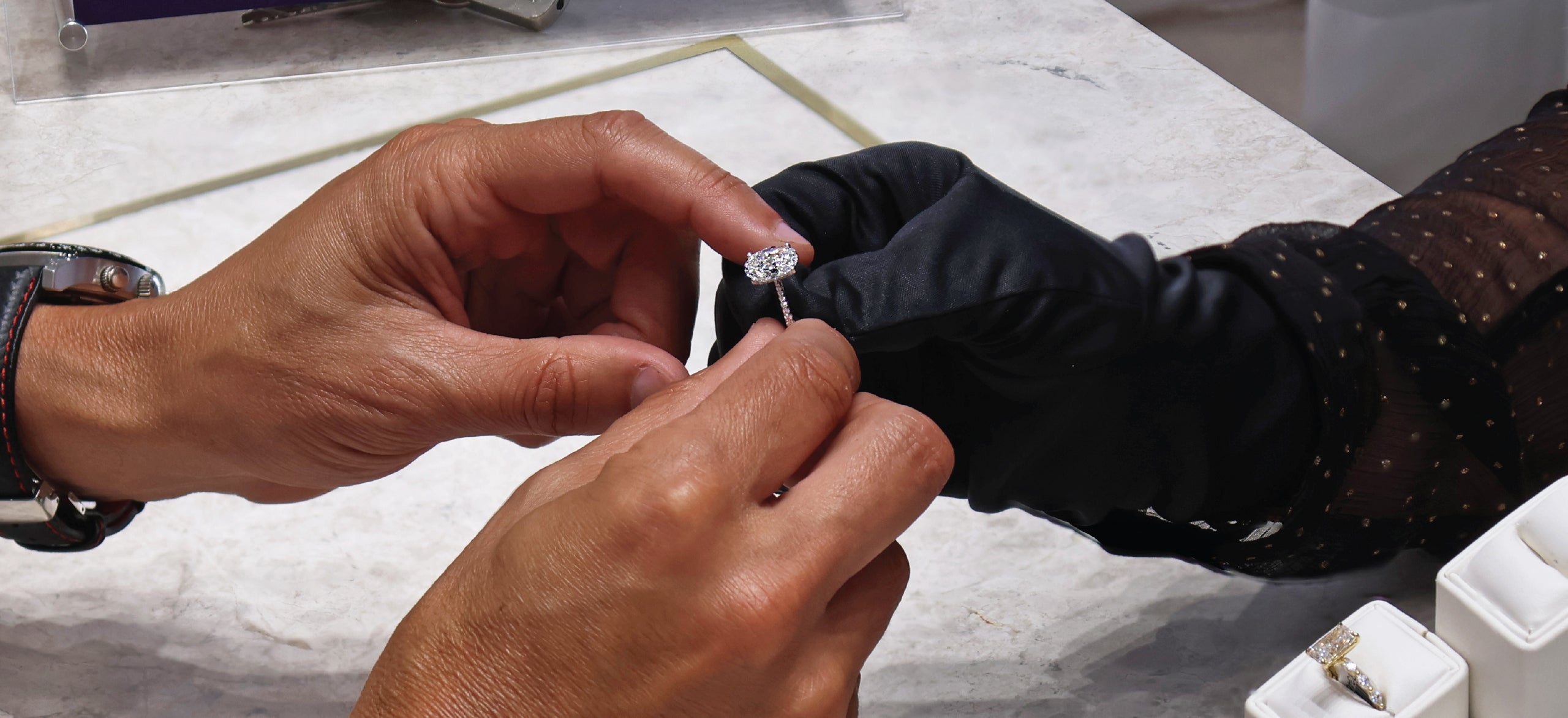 Person examining a diamond ring with another person wearing black gloves.
