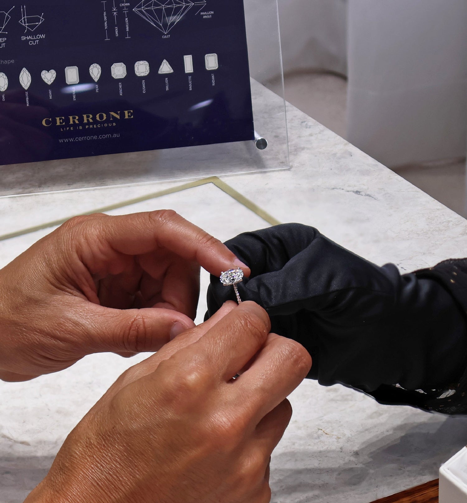Person examining a diamond ring with a Cerrone jewelry guide in the background.