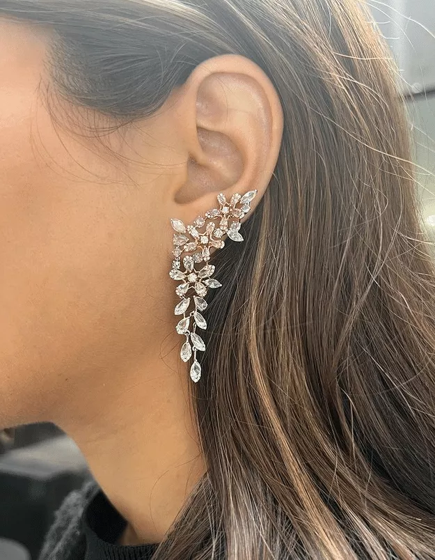 A close-up image of a woman's ear wearing a white and rose gold pink diamond drop earring.