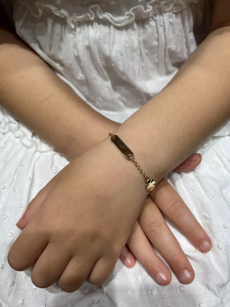 A baby's wrist wearing an 18ct yellow gold angel ID bracelet with a small loop and a gold plate with an angel figure.