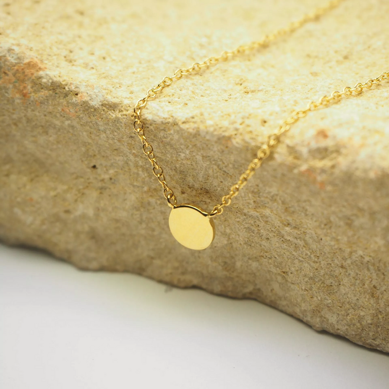 18ct yellow gold necklace with small round plate displayed on rock
