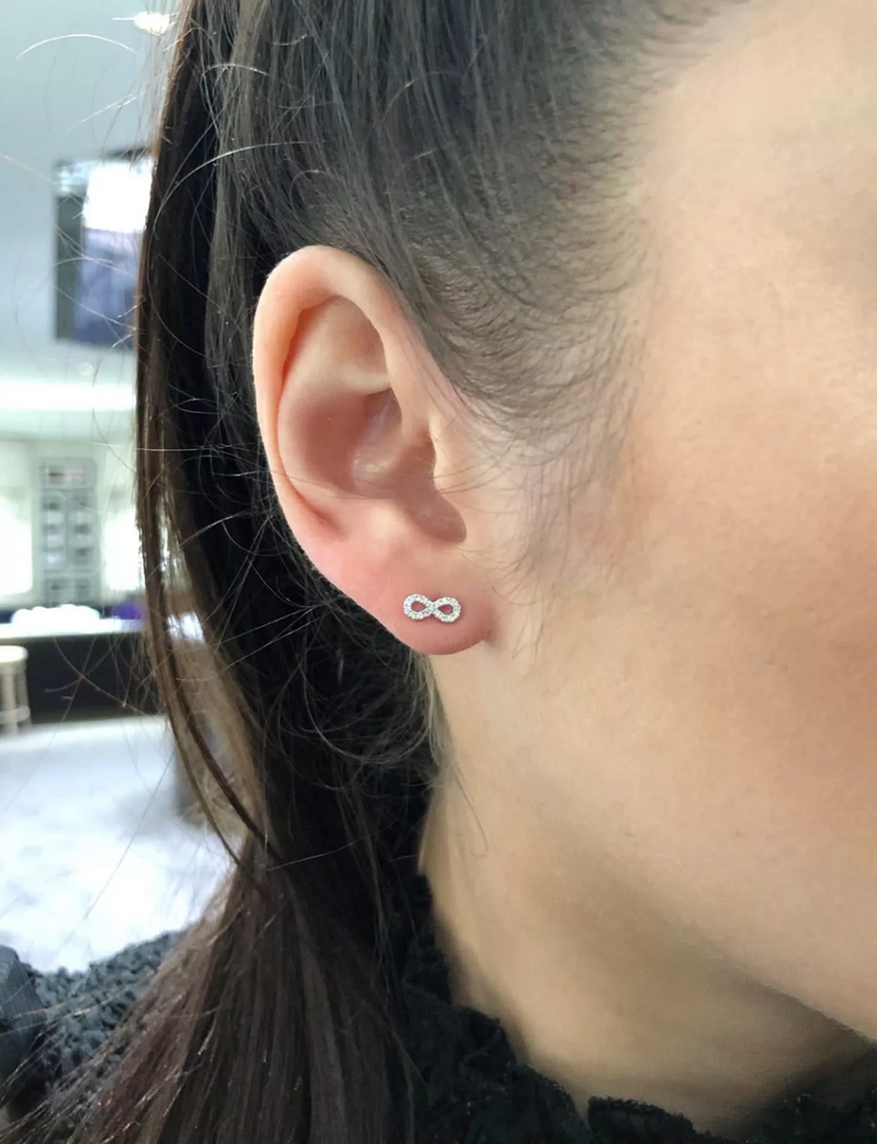 A pair of 18ct white gold small diamond infinity stud earrings with round brilliant cut diamonds on the ear