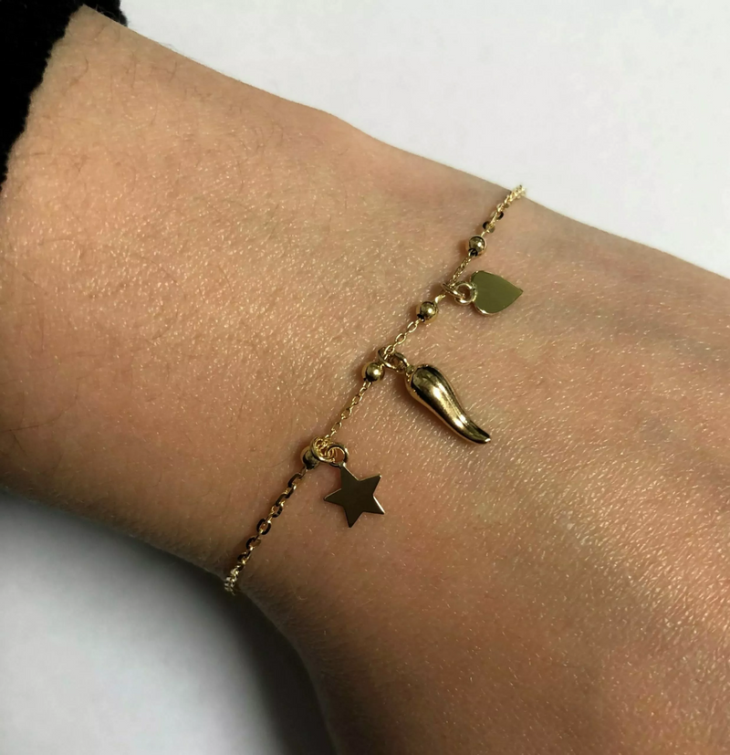 An 18ct yellow gold bracelet with a heart, corno and star charm attached to it, displayed on the wrist