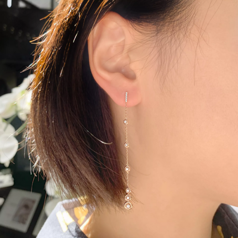 A person viewed from the side wearing 18ct rose gold drop earrings with round brilliant cut diamonds.