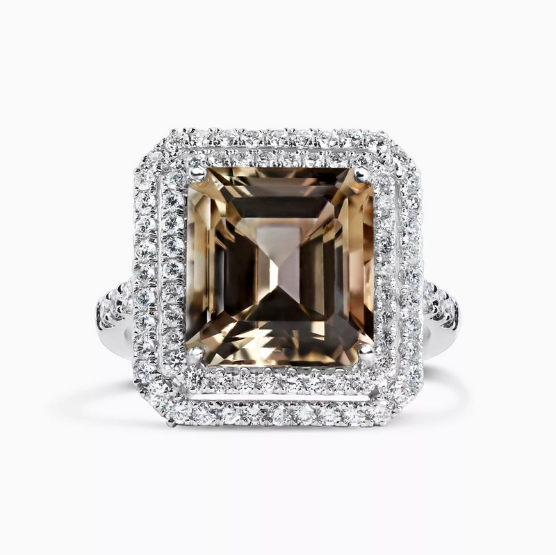 An 18ct white gold ring with an emerald cut natural light brown tourmaline centerpiece and a double halo of round brilliant cut diamonds.
