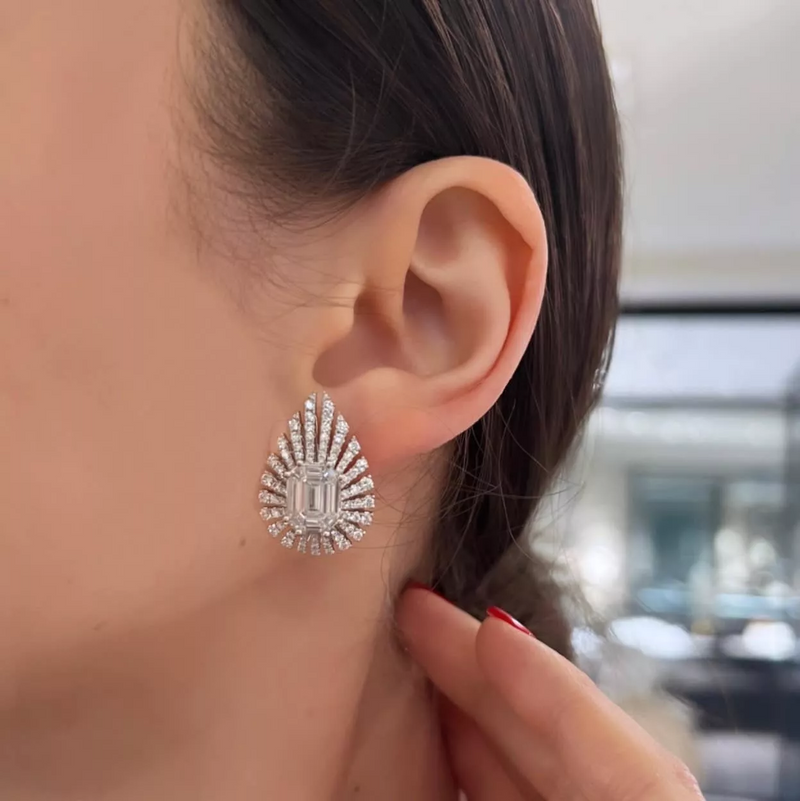 A pair of 18ct white gold baguette and round diamond earrings with a central emerald cut diamond surrounded by smaller baguette and round brilliant cut diamonds on the ear