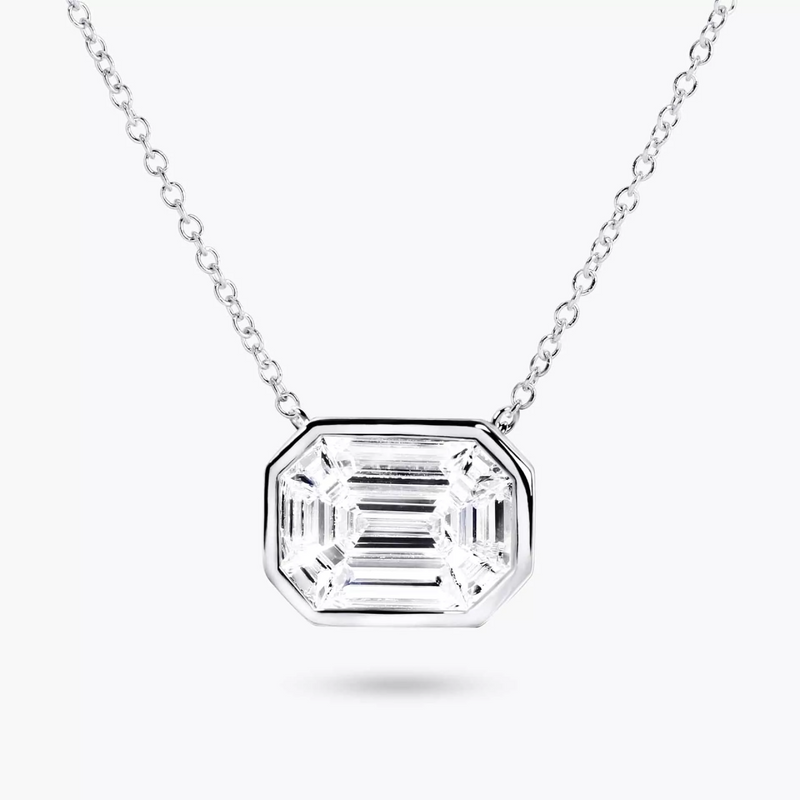 An 18ct white gold diamond necklace featuring a single, emerald-cut diamond centerpiece with a bezel setting, accompanied by a delicate chain.