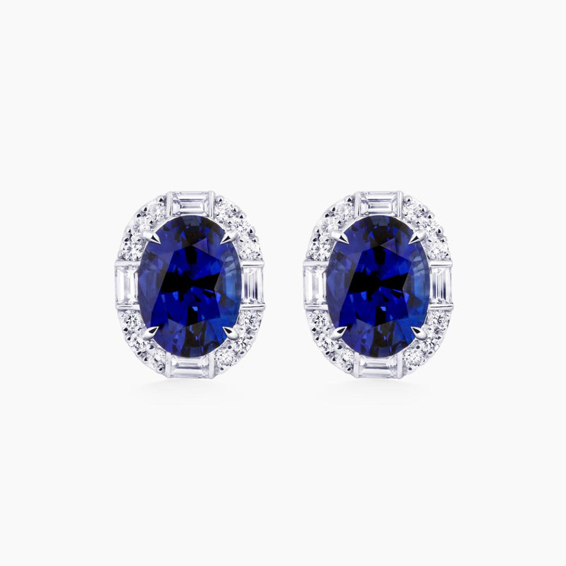 A pair of 18ct white gold earrings featuring blue Sri Lankan sapphires with a halo of round brilliant cut diamonds and baguette cut diamonds.