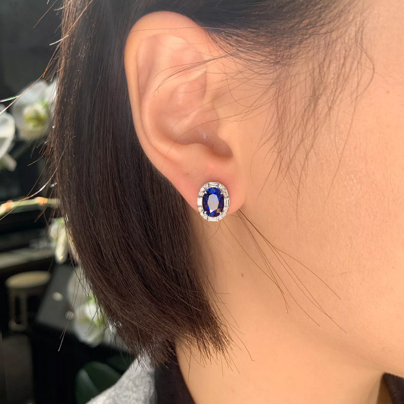 A pair of 18ct white gold earrings featuring blue Sri Lankan sapphires with a halo of round brilliant cut diamonds and baguette cut diamonds on the ear