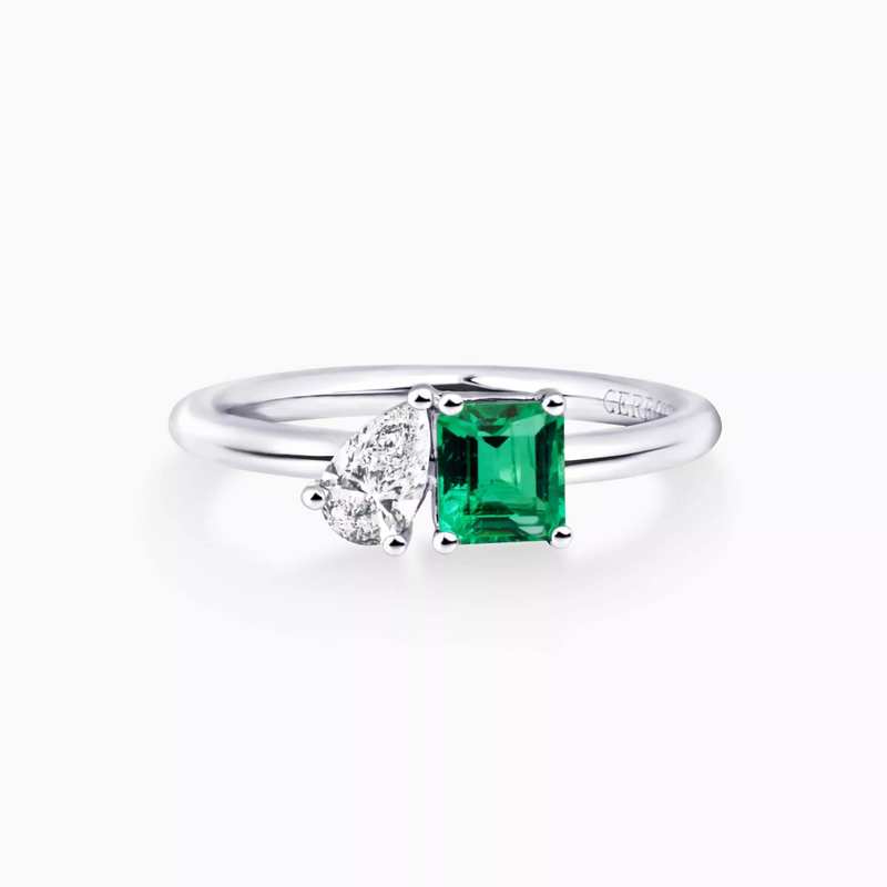 An 18ct white gold ring with an emerald cut emerald centerpiece and pear-shaped diamond accents on either side.