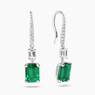 A pair of 18ct white gold drop hook earrings featuring emerald cut emeralds and round brilliant cut diamonds.