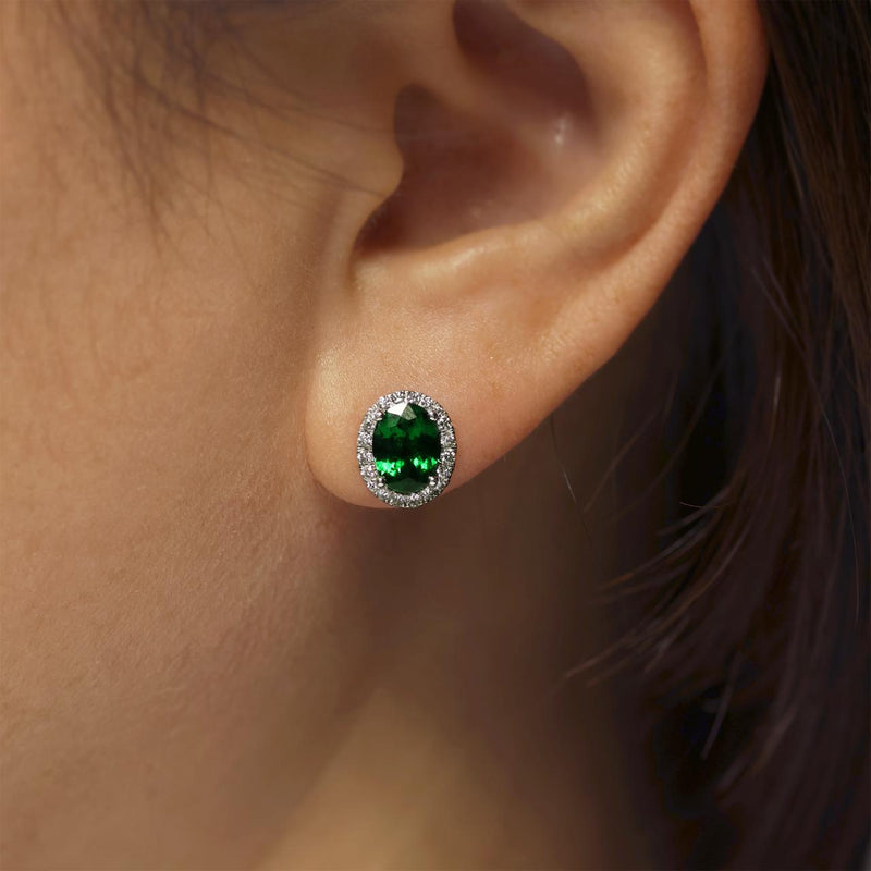 A pair of 18ct white gold oval tsavorite and round brilliant cut diamond halo stud earrings on the ear