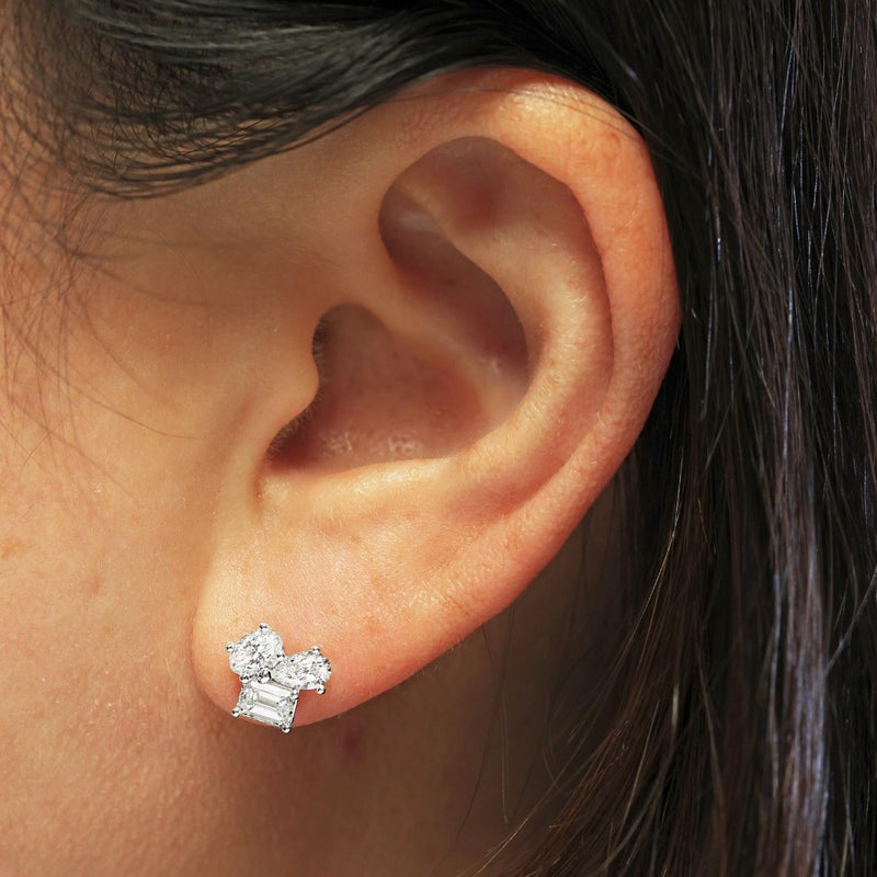 A pair of 18ct white gold diamond stud earrings featuring emerald, oval, and pear shaped diamonds in a claw setting on the ear