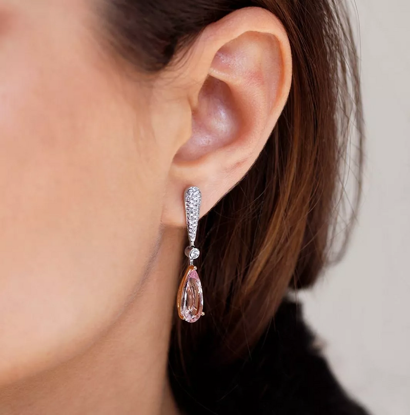 A close-up image of a woman's ear wearing a white gold, rose gold, pear-shaped morganite, and round brilliant cut diamond drop earring.