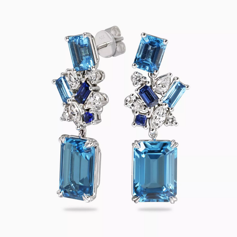 A pair of 18ct white gold drop earrings featuring emerald cut Swiss blue topaz, baguette Swiss blue topaz, princess cut Ceylon sapphire, baguette Ceylon sapphire, pear shaped diamonds, round brilliant cut diamonds, and marquise diamonds.