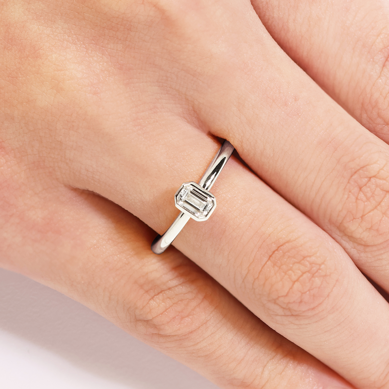 18ct white gold bezel set emerald cut diamond solitaire ring on finger