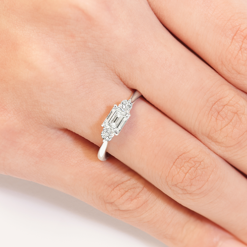18ct white gold emerald and round brilliant cut diamond engagement ring on the finger