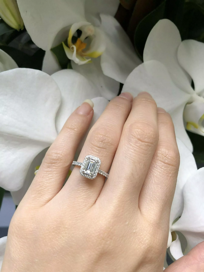 18ct white gold emerald and round brilliant cut diamond halo ring on finger