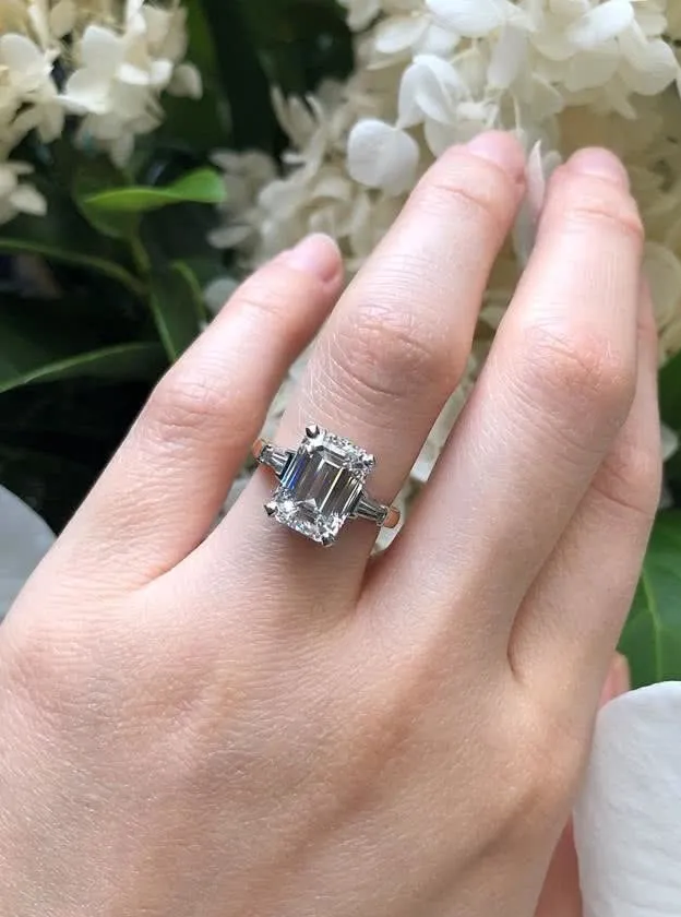 Platinum and rose gold emerald and tapered baguette trilogy ring on finger