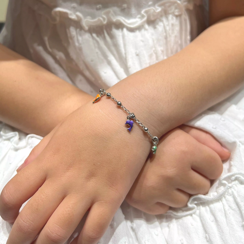 A child's wrist wearing a silver bracelet with multi-colored dolphin charms.
