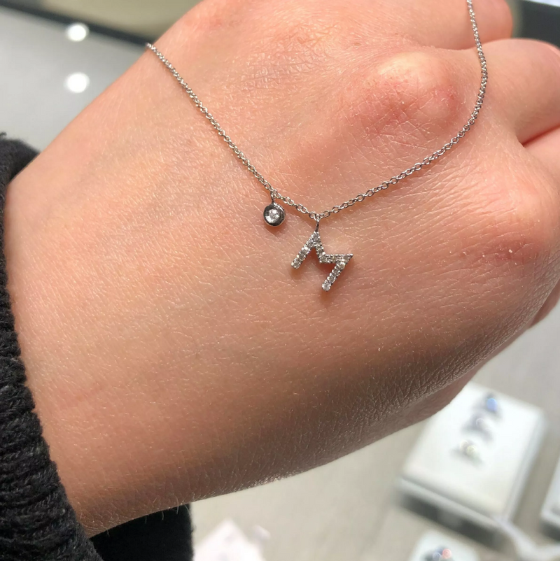 18ct white gold diamond initial “M” necklace with bezel set diamond on hand to show size of M pendant