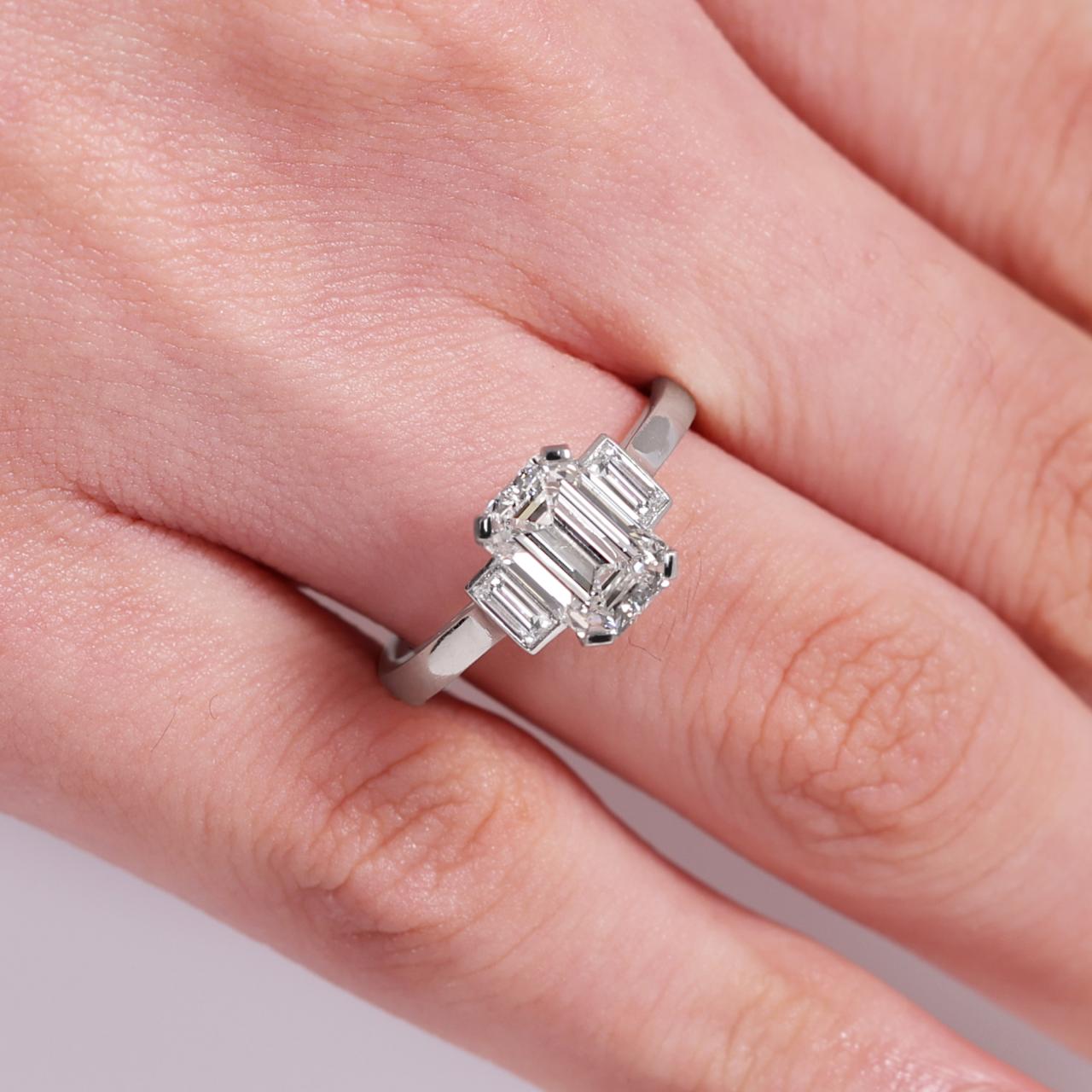 Platinum 1.81ct emerald cut diamond ring with baguette diamonds in bezel setting on the side on finger